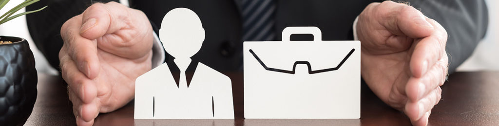 Two hands surrounding a paper cutout of a man in a suit and briefcase, on top of a desk.